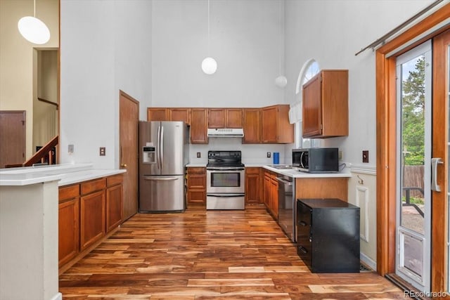13341 Birch Cir, Thornton, CO 80241 - kitchen featuring appliances with stainless steel finishes, a high ceiling, brown cabinets, wood finished floors, and under cabinet range hood