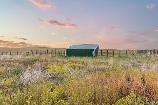 yard at dusk featuring an outbuilding, a rural view, and fence