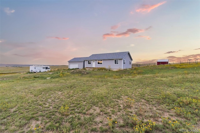 yard at dusk with an attached garage, fence, and a rural view