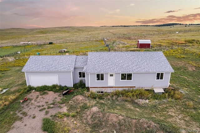 exterior space with a shingled roof, a rural view, and an attached garage