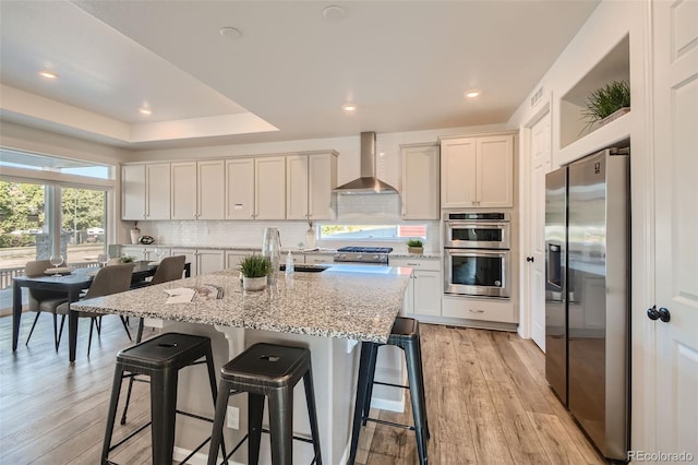 4403 Picadilly Ct, Aurora, CO 80019 - kitchen featuring appliances with stainless steel finishes, wall chimney exhaust hood, backsplash, light wood finished floors, and a breakfast bar