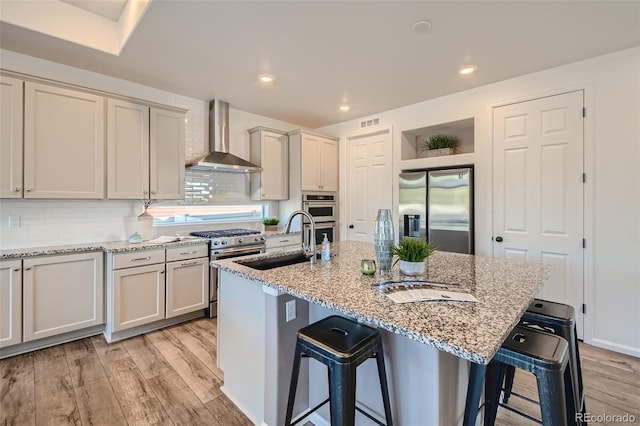 4403 Picadilly Ct, Aurora, CO 80019 - kitchen featuring appliances with stainless steel finishes, wall chimney exhaust hood, light wood-style flooring, a kitchen bar, and light stone counters