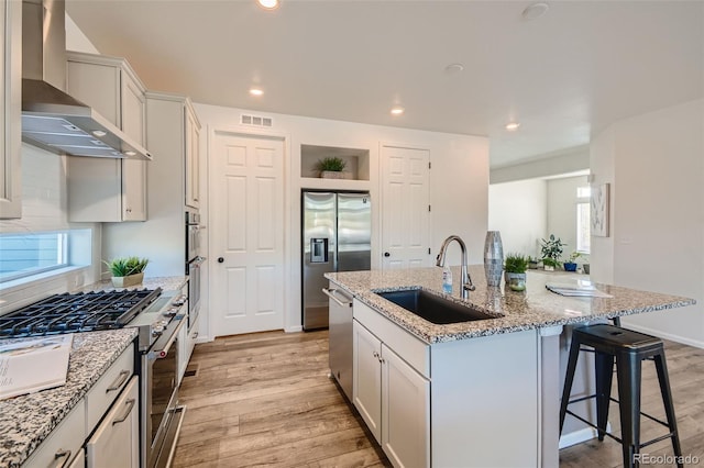 4403 Picadilly Ct, Aurora, CO 80019 - kitchen featuring wall chimney exhaust hood, appliances with stainless steel finishes, light wood finished floors, a kitchen island with sink, and a kitchen breakfast bar