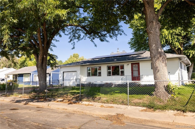 ranch-style house with a garage, a fenced front yard, and roof mounted solar panels