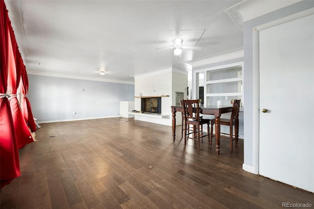 living area featuring a fireplace with raised hearth, ceiling fan, dark wood-style floors, and baseboards