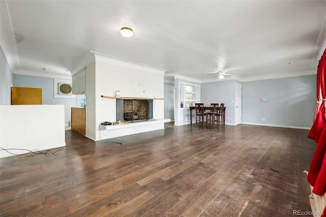 unfurnished living room with baseboards, a fireplace with raised hearth, a ceiling fan, dark wood-style flooring, and crown molding