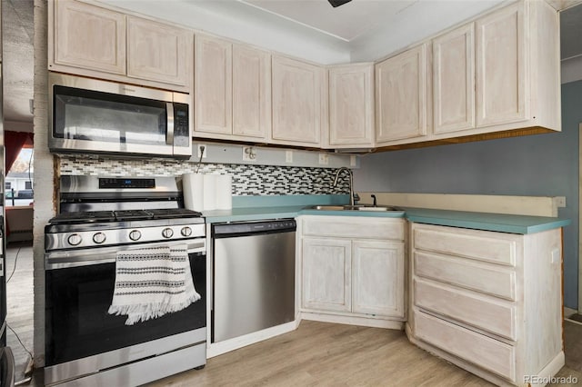 kitchen featuring stainless steel appliances, a sink, light countertops, light wood-type flooring, and backsplash