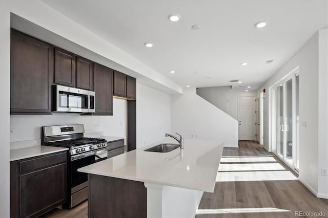 kitchen with sink, light hardwood / wood-style flooring, stainless steel appliances, dark brown cabinetry, and an island with sink