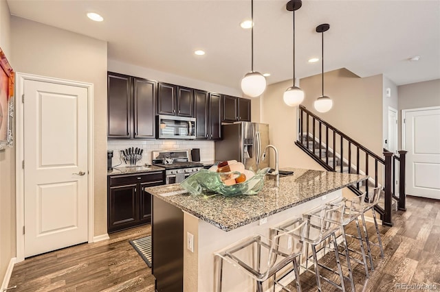 1519 S Dayton St, Denver, CO 80247 - kitchen with appliances with stainless steel finishes, wood finished floors, a kitchen bar, backsplash, and recessed lighting