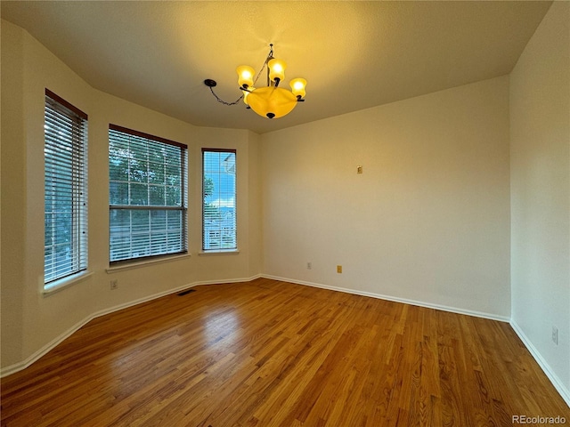 spare room featuring an inviting chandelier and hardwood / wood-style flooring