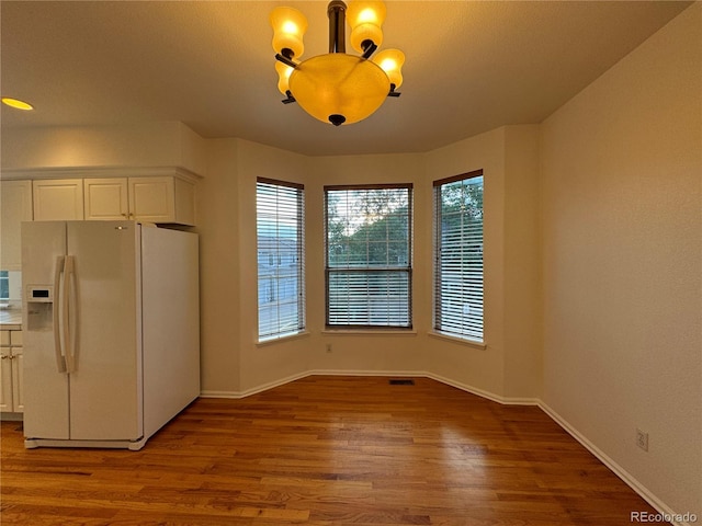 unfurnished dining area with wood-type flooring, a chandelier, and plenty of natural light