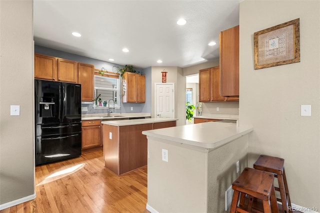 kitchen with a breakfast bar area, light countertops, black fridge with ice dispenser, a sink, and a peninsula