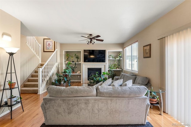 living room with light wood finished floors, stairway, a ceiling fan, and a tile fireplace