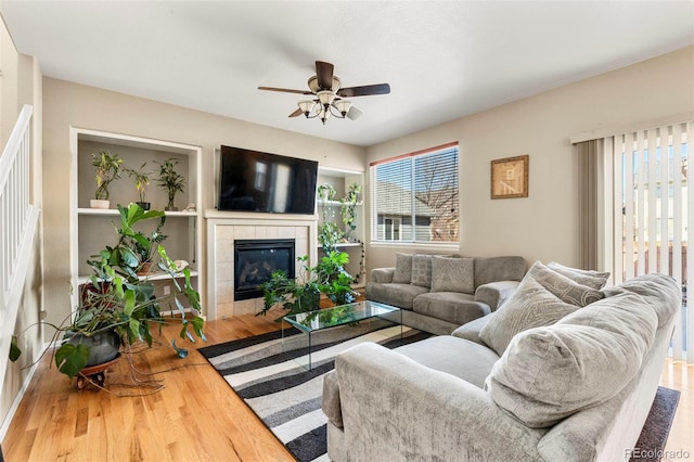 living area with ceiling fan, a tiled fireplace, and wood finished floors