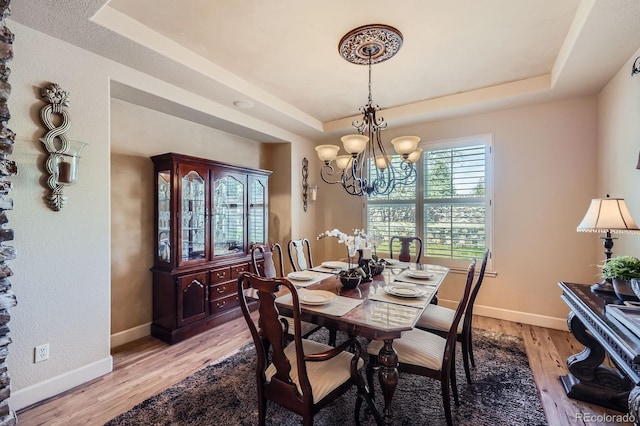 dining room with an inviting chandelier, a raised ceiling, baseboards, and light wood-style flooring