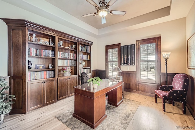 office featuring light wood-type flooring, a ceiling fan, wainscoting, and a raised ceiling