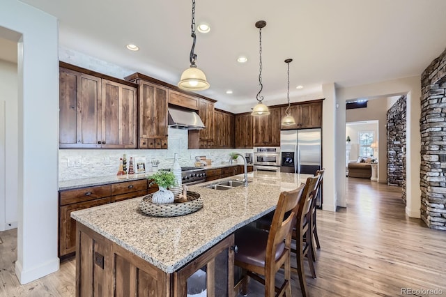 kitchen featuring a sink, a kitchen island with sink, extractor fan, light wood-type flooring, and backsplash
