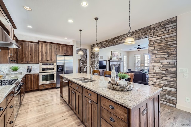 kitchen with ceiling fan, appliances with stainless steel finishes, a sink, a fireplace, and light wood-style flooring