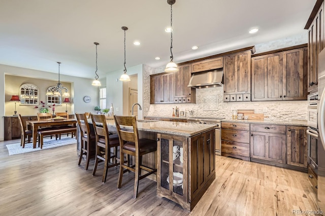 kitchen featuring decorative backsplash, range hood, stove, and an island with sink