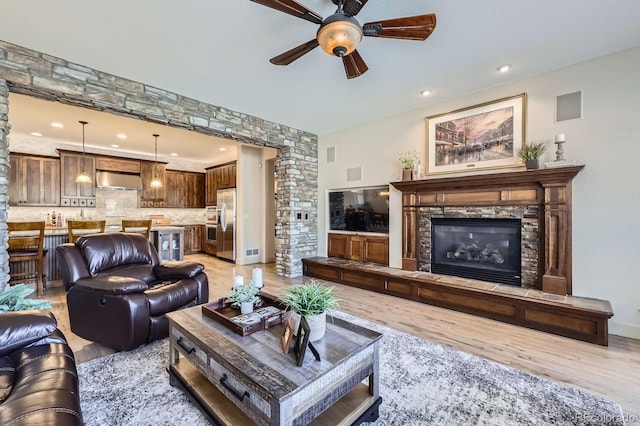 living room featuring decorative columns, a stone fireplace, a ceiling fan, and light wood-style flooring