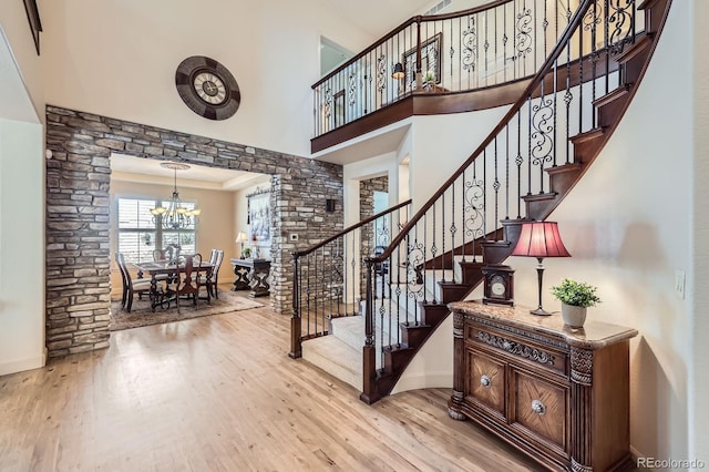 stairs with crown molding, a towering ceiling, wood finished floors, baseboards, and a chandelier