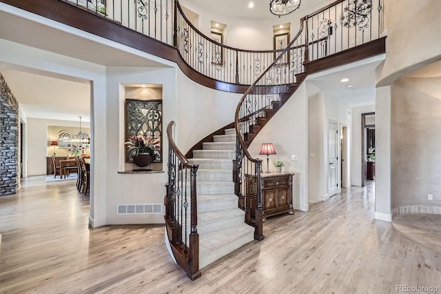 stairs featuring a towering ceiling, wood finished floors, and a notable chandelier