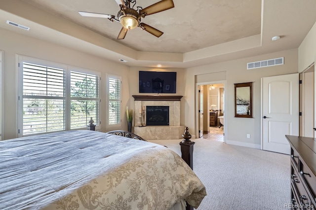 carpeted bedroom with visible vents, baseboards, a tray ceiling, and a premium fireplace