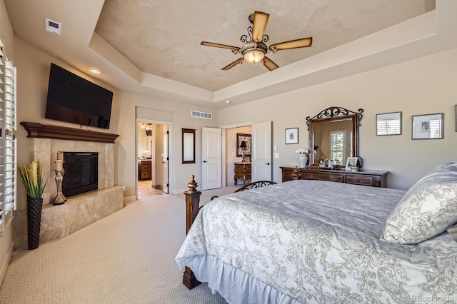 bedroom with a ceiling fan, visible vents, a raised ceiling, and a high end fireplace
