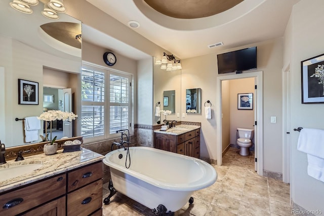 bathroom with visible vents, a freestanding tub, toilet, two vanities, and a sink