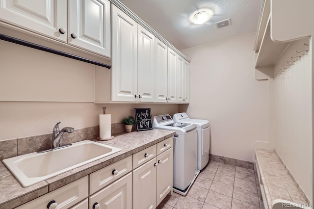 clothes washing area featuring cabinet space, washing machine and clothes dryer, a sink, light tile patterned floors, and visible vents
