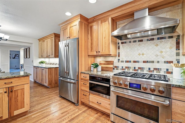 10849 E Crestridge Cir, Englewood, CO 80111 - kitchen featuring appliances with stainless steel finishes, wall chimney exhaust hood, light wood-style floors, decorative backsplash, and light stone countertops