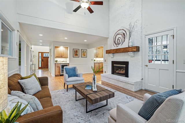 10849 E Crestridge Cir, Englewood, CO 80111 - living room featuring a large fireplace, ceiling fan, wine cooler, light wood-style flooring, and a towering ceiling