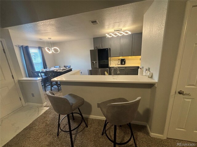 kitchen with gray cabinetry, a breakfast bar, kitchen peninsula, and black refrigerator with ice dispenser