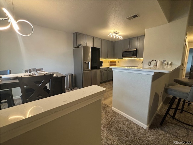 kitchen featuring kitchen peninsula, appliances with stainless steel finishes, a kitchen breakfast bar, a textured ceiling, and gray cabinets