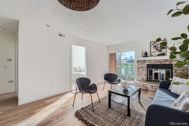 living room featuring a fireplace, light wood finished floors, visible vents, a textured ceiling, and baseboards