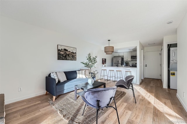 living area with stacked washing maching and dryer, baseboards, and light wood-style floors