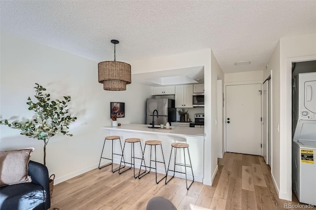 kitchen with light wood-style flooring, appliances with stainless steel finishes, a kitchen breakfast bar, stacked washer / drying machine, and a textured ceiling