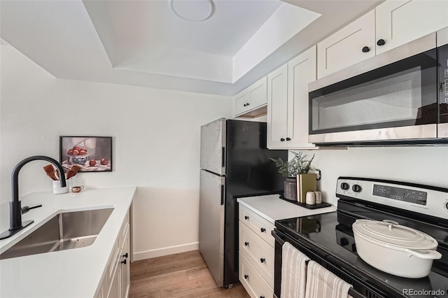 kitchen with stainless steel appliances, a sink, white cabinetry, light wood finished floors, and a raised ceiling