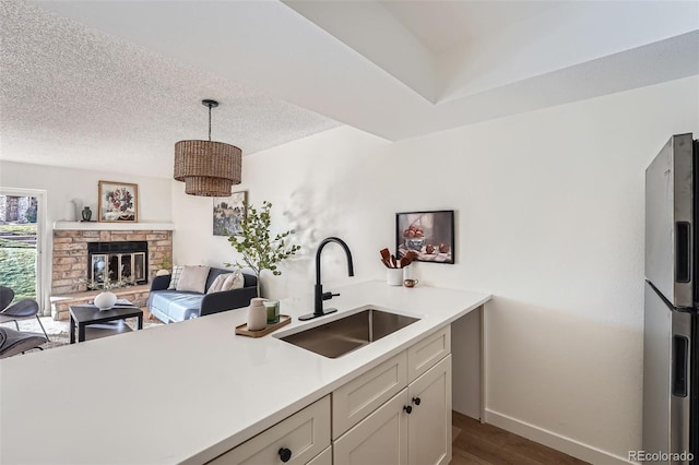 kitchen with a textured ceiling, a stone fireplace, a sink, light countertops, and stainless steel refrigerator with ice dispenser