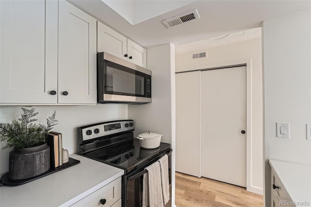 kitchen featuring stainless steel appliances, white cabinetry, visible vents, light wood-style floors, and light countertops