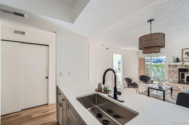 kitchen with a textured ceiling, a sink, visible vents, light wood-style floors, and open floor plan