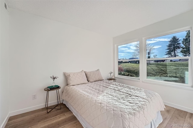 bedroom featuring light wood-style flooring, visible vents, baseboards, and a textured ceiling