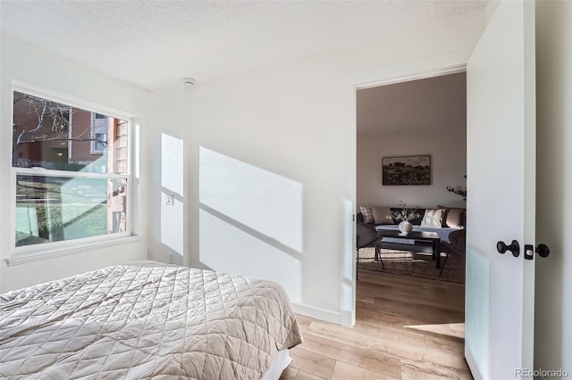 bedroom featuring light wood-style flooring, a textured ceiling, and baseboards