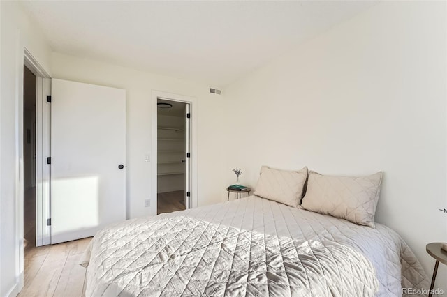 bedroom featuring light wood finished floors, visible vents, and a walk in closet