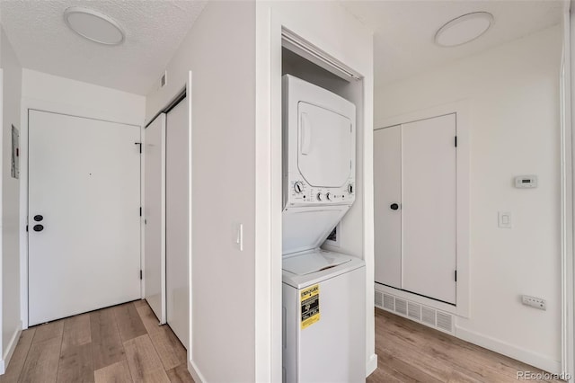 laundry area with a textured ceiling, light wood-style flooring, laundry area, visible vents, and stacked washer and clothes dryer