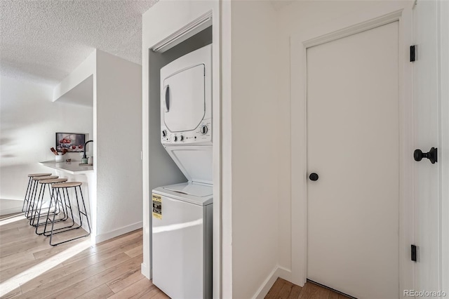 laundry room featuring laundry area, light wood finished floors, baseboards, stacked washer and clothes dryer, and a textured ceiling