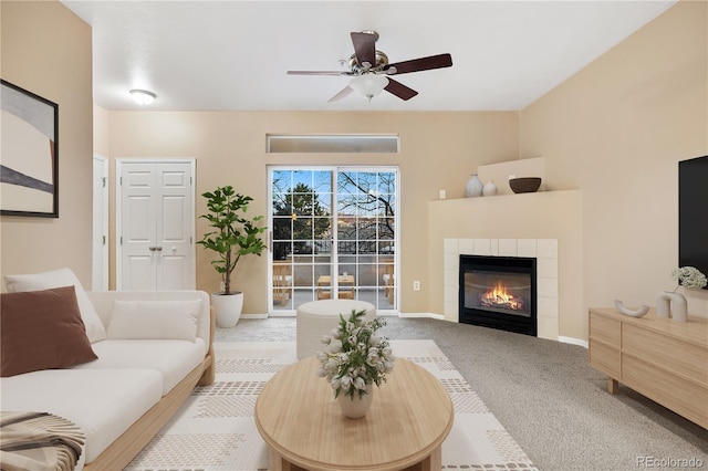 living room with carpet, ceiling fan, a tiled fireplace, and baseboards