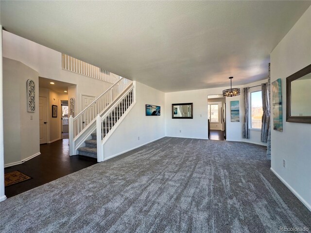 unfurnished living room with dark colored carpet and a notable chandelier