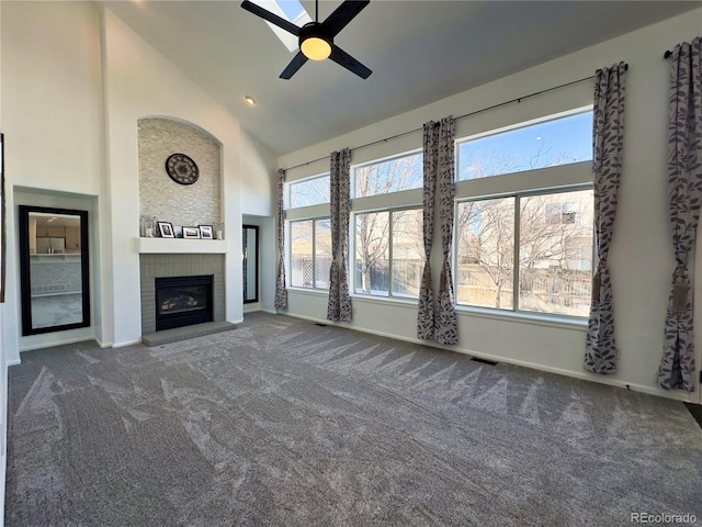 unfurnished living room featuring ceiling fan, high vaulted ceiling, a brick fireplace, and dark colored carpet