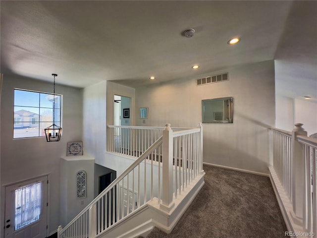 hallway featuring a notable chandelier and dark colored carpet